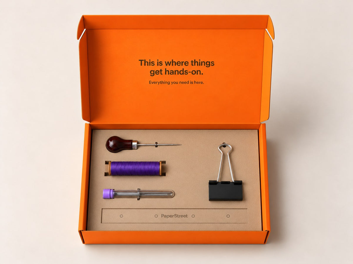 Open orange Journal Binding Kit with papers, waxed thread, needle, awl and binder clips